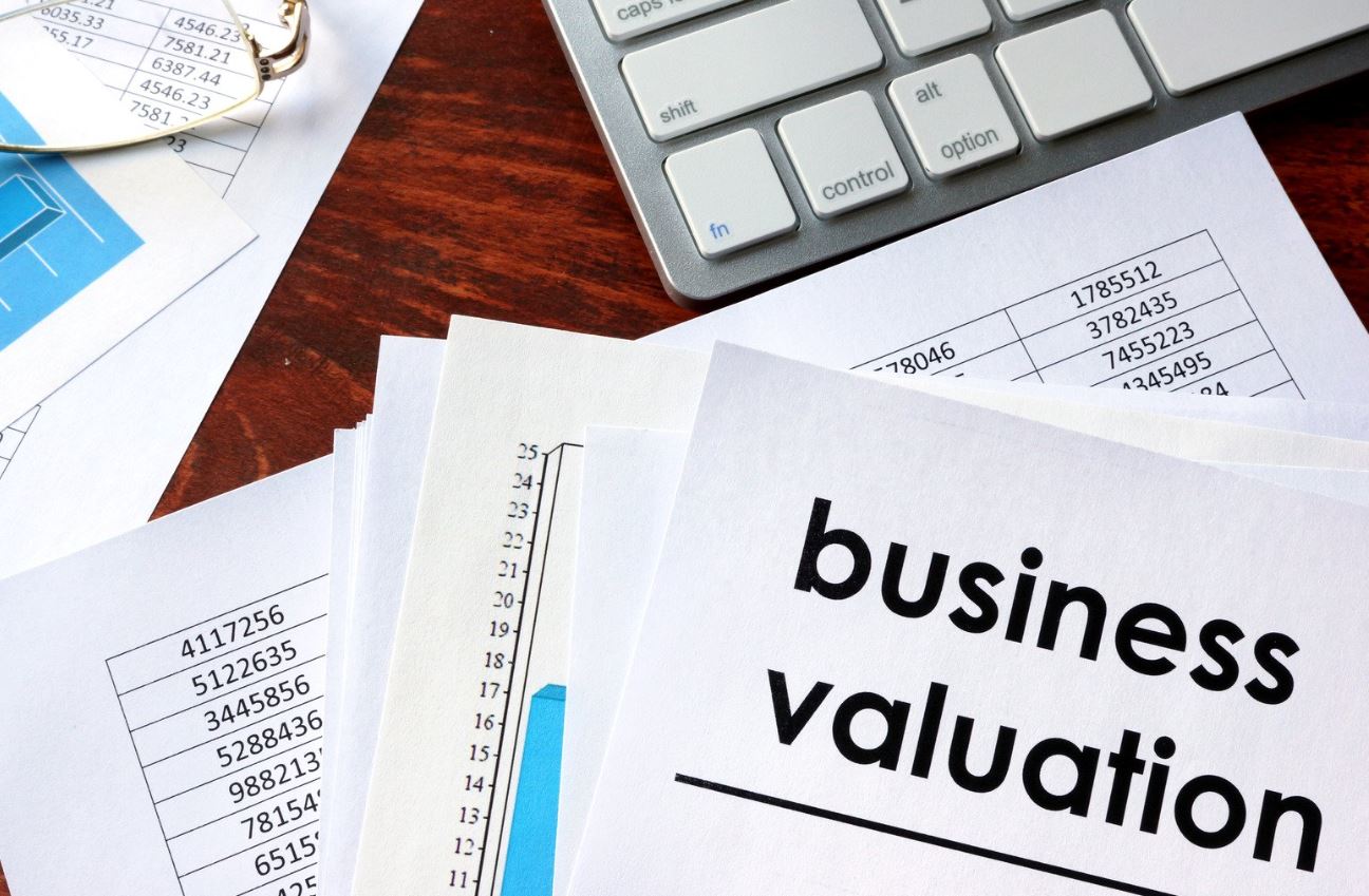 A close-up view of a desk featuring a stack of documents labeled "business valuation," alongside financial tables and a computer keyboard. The image highlights the importance of business valuation in financial analysis, showcasing various numerical data and charts that support decision-making processes. This visual representation emphasizes the analytical aspect of evaluating a business's worth.